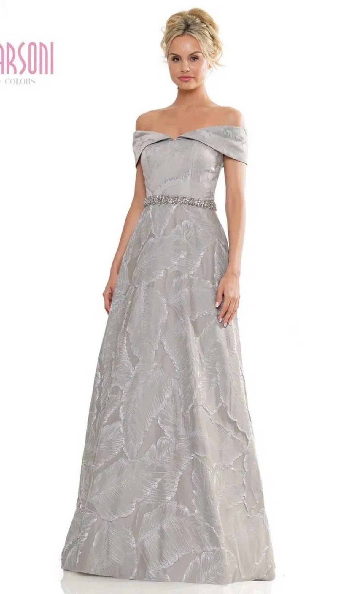 A woman models the Charcoal Marsoni MV1265 long formal dress featuring an off-the-shoulder design, patterned texture, and beaded waistline against a plain white background.